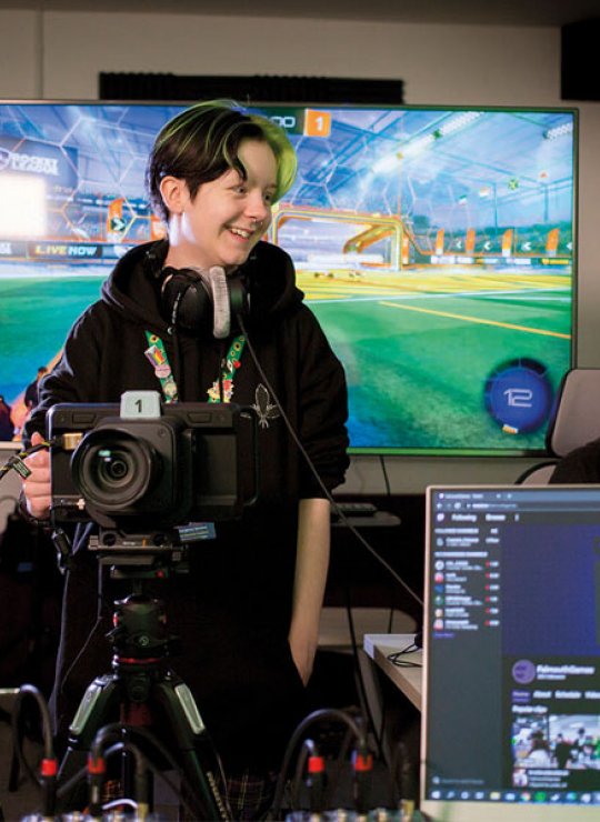 Esports students stood in front of digital screens with cameras